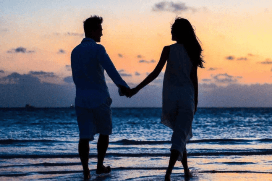 ζευγάρι περπατάει χέρι χέρι στη θάλασσα στο ηλιοβασίλεμα